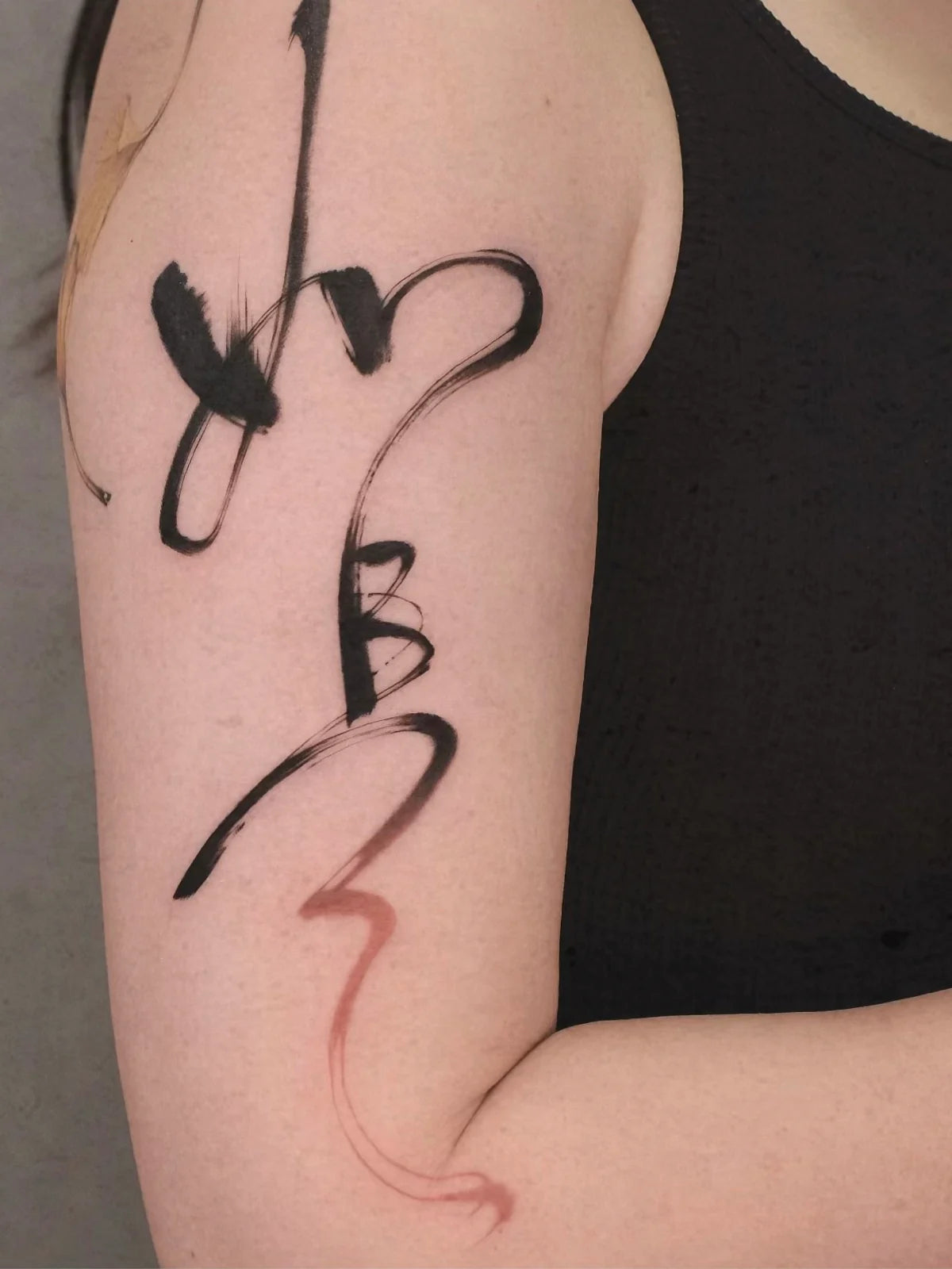 Flowing black and red Chinese calligraphy tattoo on an upper arm