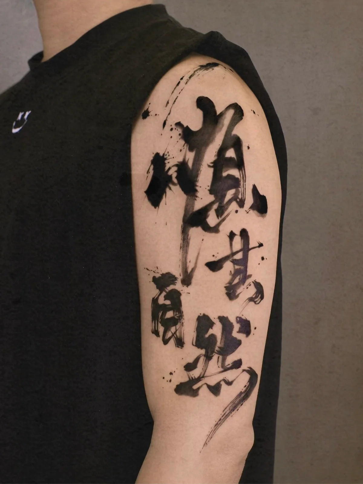 Expressive black Chinese brush calligraphy tattoo on an upper arm