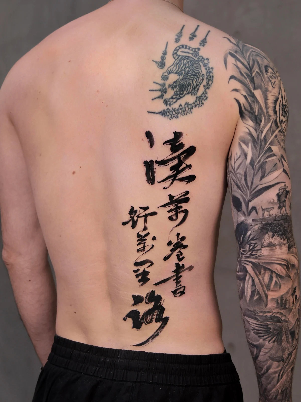 Large Chinese calligraphy tattoo across the back beside existing shoulder and sleeve tattoos