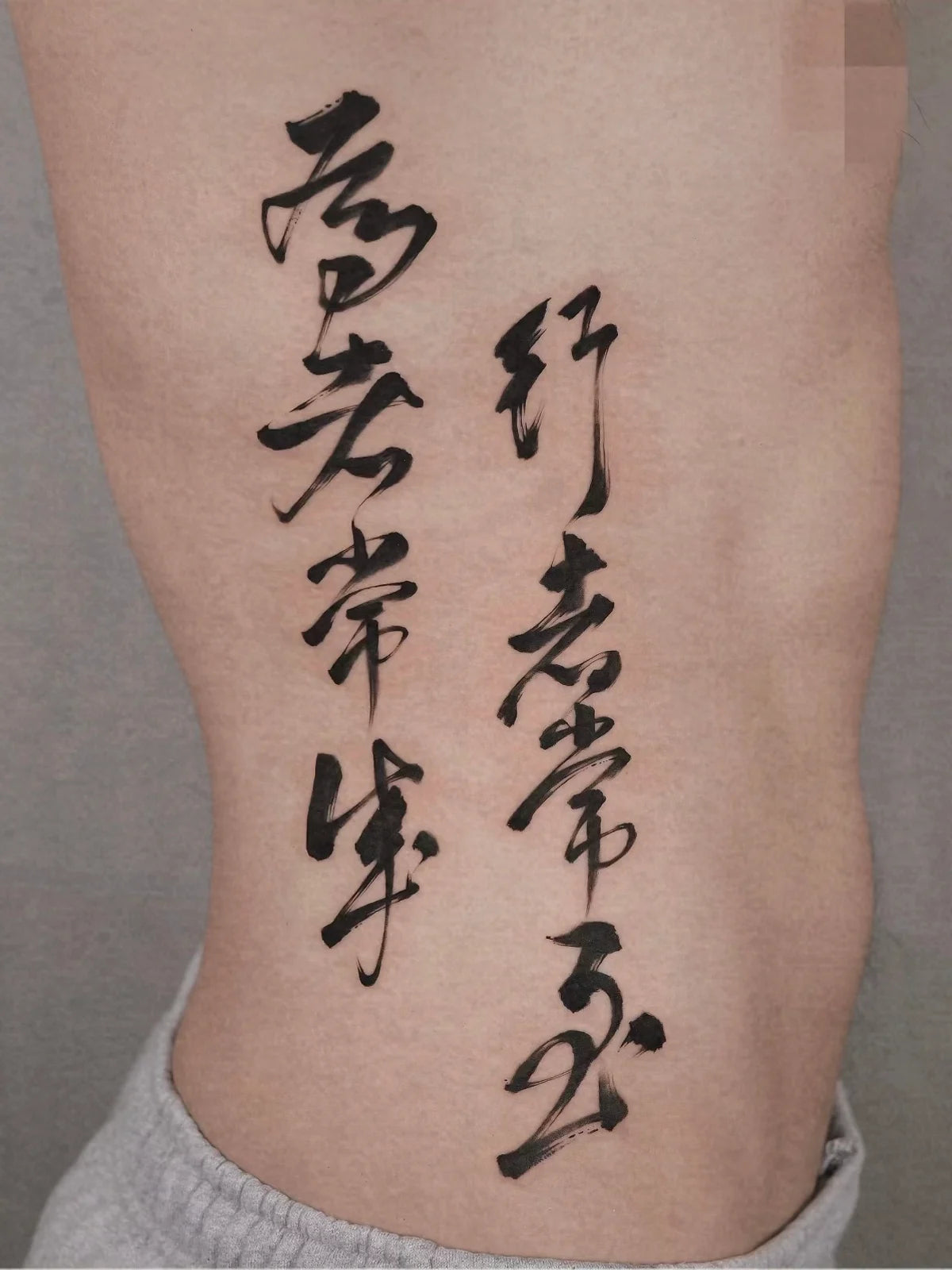 Two-column black Chinese calligraphy tattoo on the side of the torso