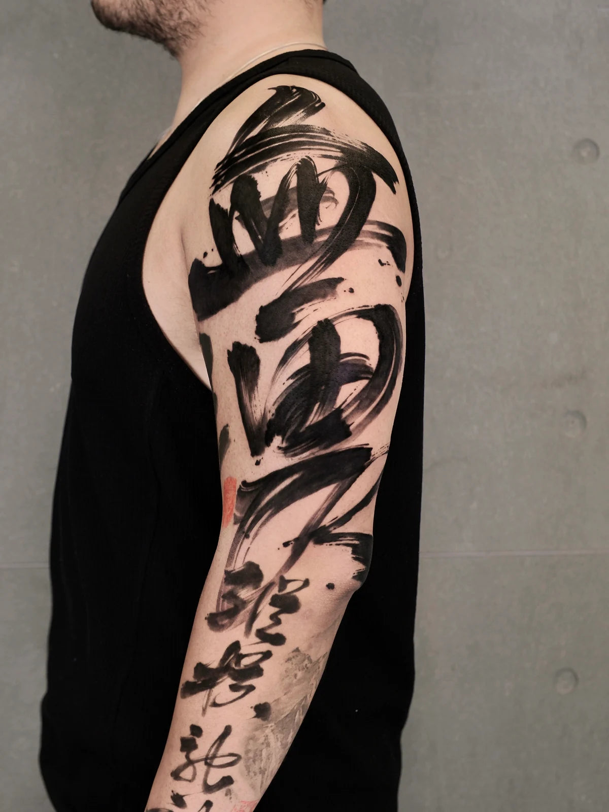 Bold black Chinese brush calligraphy extending from the shoulder down the arm, with small red accents